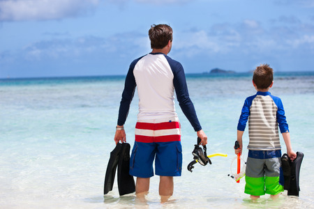 Back view of father and son with snorkeling equipment fins and mask at tropical beachの写真素材