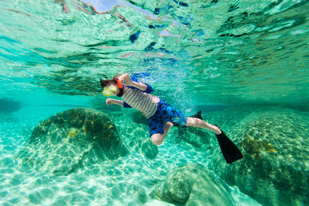 Cute teenage boy swimming underwater in shallow turquoise water at tropical beachの写真素材