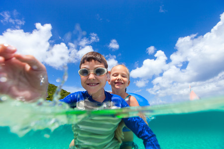Adorable little girl and cute boy splashing in a tropical ocean water during summer vacationの写真素材