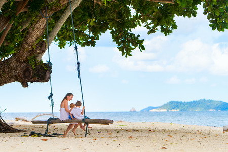 Mother with two kids having fun swinging at tropical beachの写真素材
