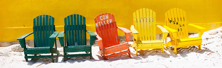 Row of colorful wooden chairs at tropical white sand beach in Caribbean agains colorful wallの写真素材