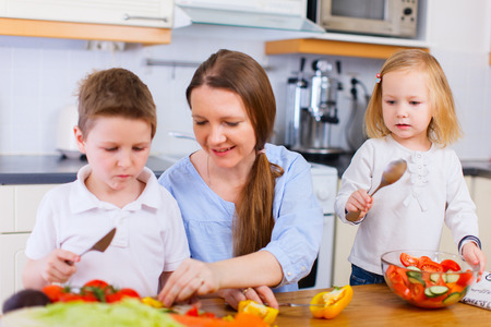 Young mother and her two kids making vegetable saladの写真素材