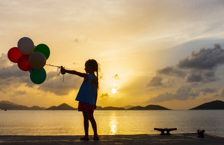 Silhouette of adorable happy little girl with bunch of balloons on sea coast at sunsetの写真素材