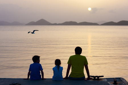 Back view family silhouettes on tropical coast at sunsetの写真素材