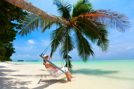 Young beautiful woman relaxing in swing hanging on coconut palm at tropical beachの写真素材