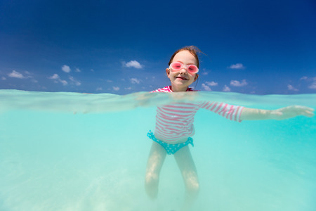 Split underwater and above photo of a little girl splashing in tropical oceanの写真素材