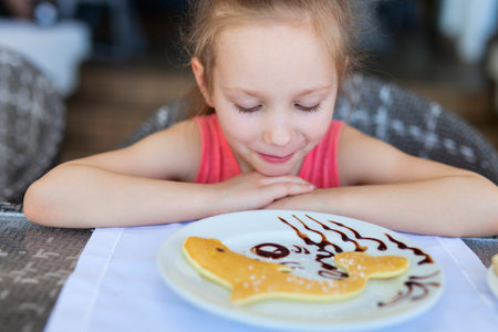 Adorable little girl eating pancake for a breakfast in restaurantの写真素材