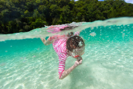 Split underwater and above photo of a little girl splashing in tropical ocean