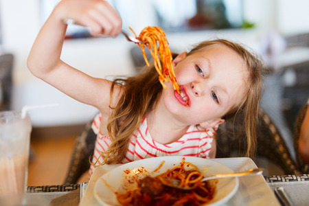 Portrait of adorable little girl eating spaghetti for a lunch at restaurantの写真素材
