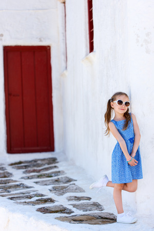 Charming little girl at typical greek traditional village with white houses and colorful doors on Mykonos Island, Greece, Europeの写真素材