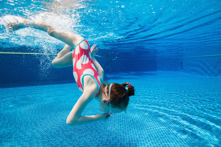 Underwater photo of adorable little girl diving and swimming in pool on summer vacation