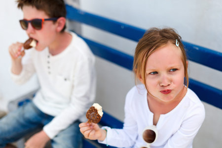 Two adorable kids eating ice cream outdoors on a hot summer dayの写真素材