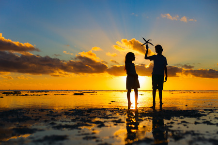 Silhouettes of kids brother and sister  holding starfish at tropical beach during sunsetの写真素材