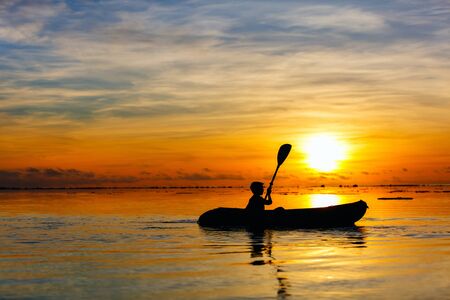 Silhouette of a boy paddling at tropical ocean at sunsetの写真素材