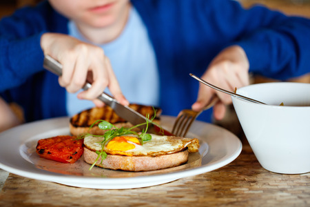 Boy eating fried egg on toast and porridge for breakfastの写真素材