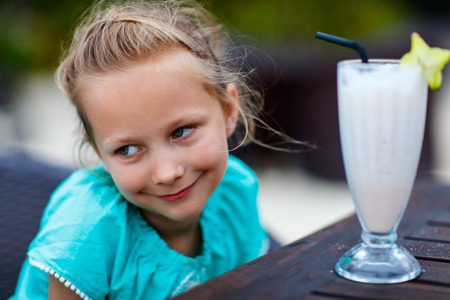Adorable little girl drinking fresh smoothie at outdoor cafe on summer dayの写真素材