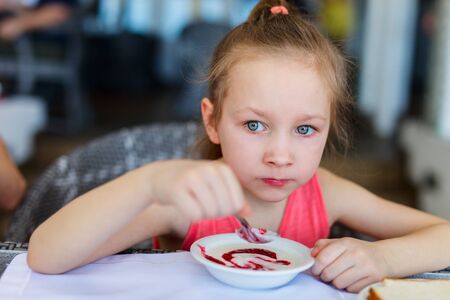 Adorable little girl eating breakfast in restaurantの写真素材