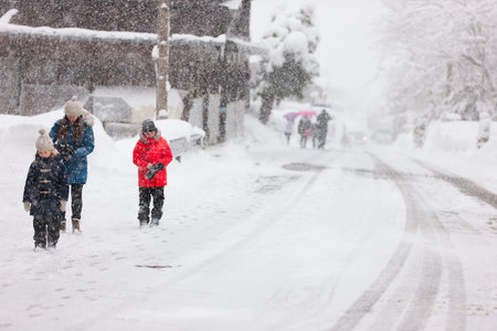 Family of mother and kids outdoors on cold winter day walking under heavy snowfall