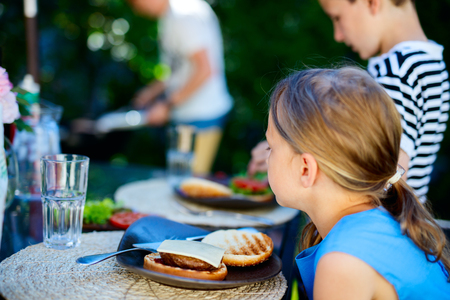 Adorable little girl and her family eating delicious homemade burger outdoors on summer dayの写真素材