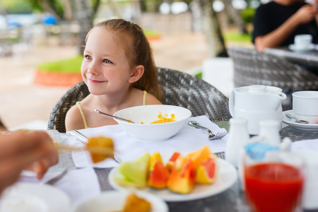 Adorable little girl eating cereal with milk for breakfast in restaurantの写真素材