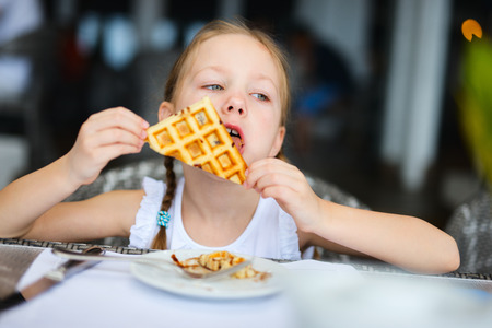 Adorable little girl eating waffle for a breakfast in restaurantの写真素材