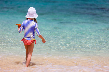 Little girl in a colorful sun protection swimwear on vacation splashing in a shallow water at tropical beachの写真素材