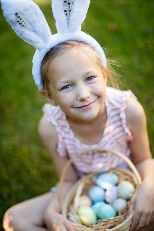 Adorable little girl wearing bunny ears holding a basket with Easter eggs outdoors on spring dayの写真素材