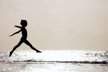 Silhouette of adorable little girl on a beach at sunsetの写真素材