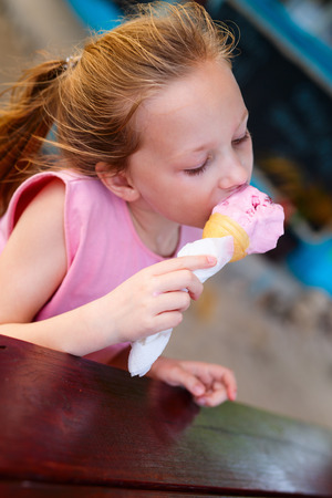 Adorable little girl eating ice cream in a fresh waffle cone in outdoor cafe on summer dayの写真素材