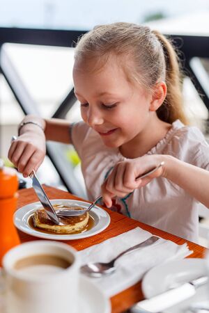Adorable little girl eating pancake for breakfast in restaurantの写真素材