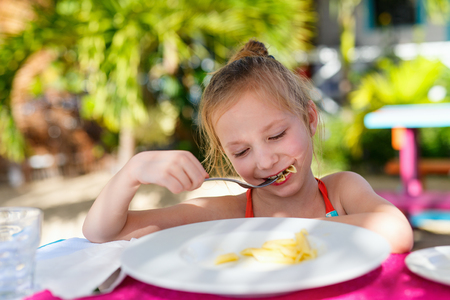 Portrait of adorable little girl eating pasta for a lunch at restaurantの写真素材
