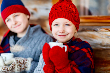 Kids outdoors on beautiful winter day drinking hot chocolate in front of log cabin vacation houseの写真素材