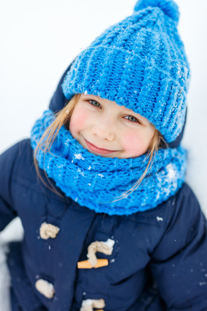 Adorable little girl wearing warm clothes outdoors on beautiful winter snowy dayの写真素材