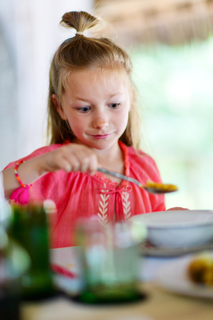 Adorable little girl eating cereal with milk for breakfast in restaurant or at homeの写真素材