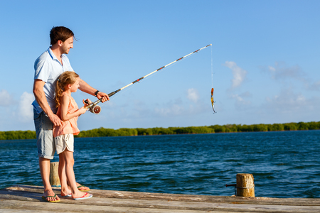 Family father and daughter fishing together from wooden jetty