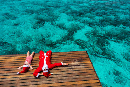 Christmas Santa Claus and little girl enjoying xmas travel vacation at tropical oceanの写真素材