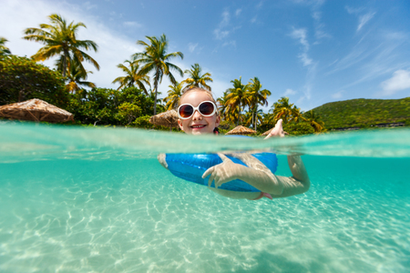Split underwater and above photo of a little girl swimming in a tropical ocean with inflatable ringの写真素材