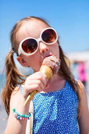 Adorable little girl eating ice cream in a fresh waffle cone outdoors on summer dayの写真素材