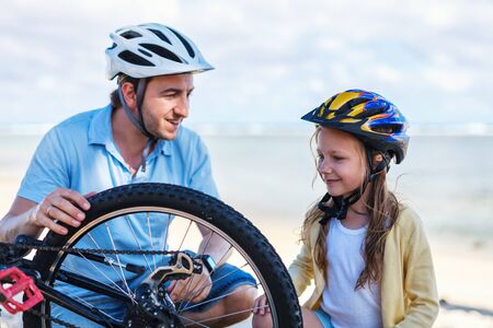 Little girl and her father repairing bicycle outdoors at summerの写真素材