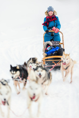 Husky dogs are pulling sledge with family at winter forest in Lapland Finlandの写真素材