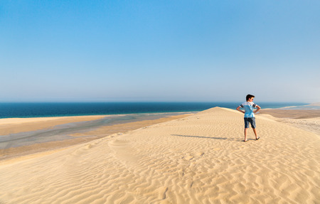 Teenage boy having fun playing at sand dunes in Qatar desertの写真素材