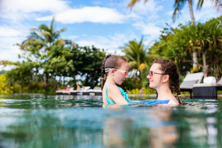 Happy mother and her adorable little daughter outdoors in the swimming pool at tropical resortの写真素材