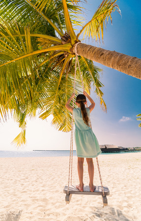 Adorable girl having fun swinging at tropical island beachの写真素材