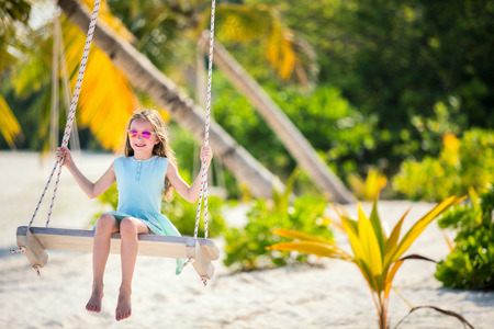 Adorable girl having fun swinging at tropical island beachの写真素材