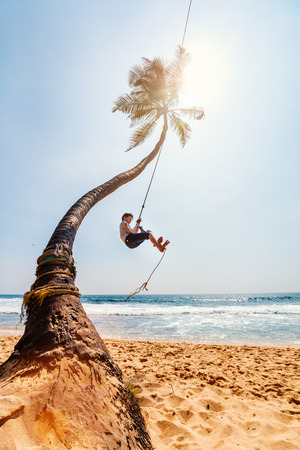 Cute teenage boy having fun swinging on a rope at tropical island beach in Sri Lankaの写真素材