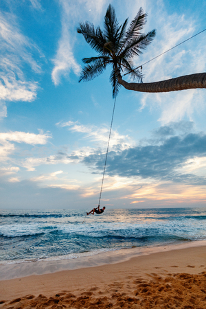 Cute teenage boy having fun swinging on a rope at tropical island beach in Sri Lankaの写真素材