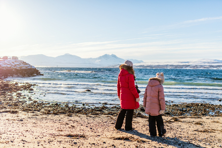 Beautiful family of mother and kids enjoying snowy winter day outdoors at beach surrounded by fjords in Northern Norwayの写真素材