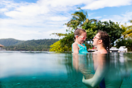 Happy mother and her adorable little daughter outdoors in the swimming pool at tropical resort