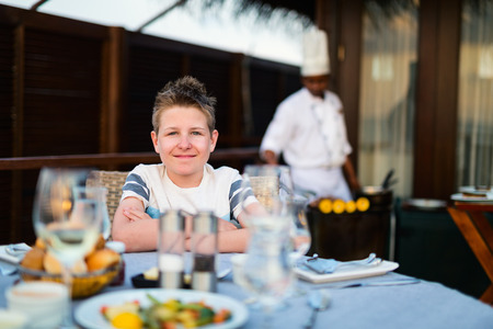 Cute teenage boy having dinner at outdoor restaurant on summer dayの写真素材