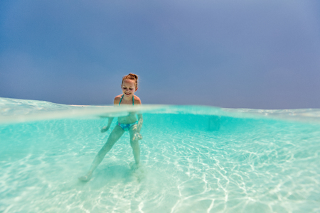 Split underwater and above photo of a little girl splashing in tropical oceanの写真素材